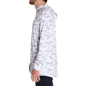 A man stands in profile facing left against a plain white background, wearing the Icelantic UV Sun Hoodie - Snow Camo, a light gray and white camouflage sun protective hoodie with UPF 50 and quick-dry fabric, paired with black pants. This hoodie combines reliable sun protection with modern style.