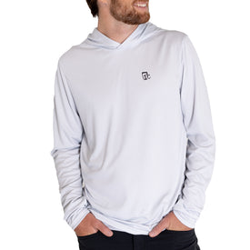 A man stands with his hands in his pockets and smiles against a white background, wearing the Icelantic UV Sun Hoodie - Cowboy in light gray, which features a small black logo on the chest and provides UPF 50 sun protection.