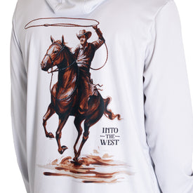 A person wearing the Icelantic UV Sun Hoodie - Cowboy, a white sun-protective hoodie featuring an illustration of a cowboy riding a horse and swinging a lasso above the text INTO THE WEST. This stylish hoodie provides UPF 50 sun protection, making it perfect for all your outdoor adventures.