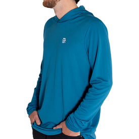 A person wearing the Icelantic UV Sun Hoodie in Celestial Teal, featuring long sleeves, UPF 50 sun protection, and a small white Icelantic logo on the chest, stands with hands in pockets facing sideways against a white background.
