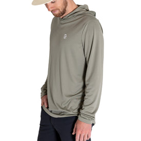 A man wearing the Icelantic UV Sun Hoodie in Olive Grey, featuring UPF 50 sun protection, paired with dark pants and looking down with one hand by his side against a plain white background.