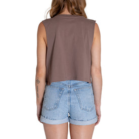 A person with long hair, wearing the Icelantic Cactus Cropped Tank - Musk and light blue denim shorts, is shown from the back. A small tattoo is visible on their left arm. The plain white background highlights this effortlessly cool piece of summer gear.