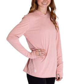 A woman wearing the Icelantic Womens UV Sun Hoodie - Cowgirl in light pink, featuring long sleeves and UPF 50 sun protection, paired with black pants and rings, stands with one hand on her hip against a white background.
