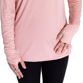 A person is wearing the Icelantic Womens UV Sun Hoodie - Cowgirl, a long-sleeve pink top featuring thumb holes, paired with black leggings. Only the torso and hands are visible, adorned with several rings, including a turquoise ring. The quick-dry fabric of this hoodie ensures all-day comfort, making it a practical yet stylish choice.