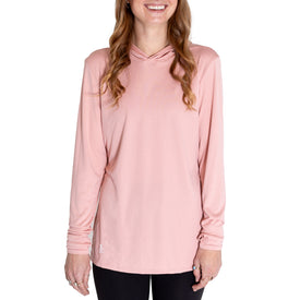 A woman with wavy hair is smiling as she stands against a white background, wearing the Icelantic Womens UV Sun Hoodie - Cowgirl in light pink along with black pants.