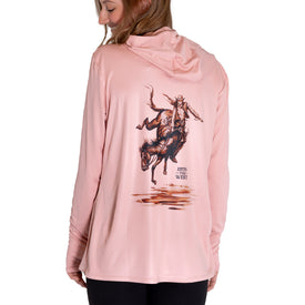 A woman wears the Icelantic Womens UV Sun Hoodie - Cowgirl, a light pink sun-protective hoodie featuring UPF 50 protection, with an illustration of a cowboy riding a bucking horse and the words “Into the West” on the back—keeping you stylish and shielded from harmful rays.