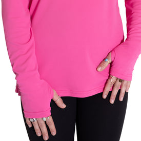 A person wears the Icelantic Womens UV Sun Hoodie in hot pink—a UPF 50 long-sleeve shirt with thumb holes—paired with black pants, displaying hands adorned with several rings. Only the torso and hands are visible.