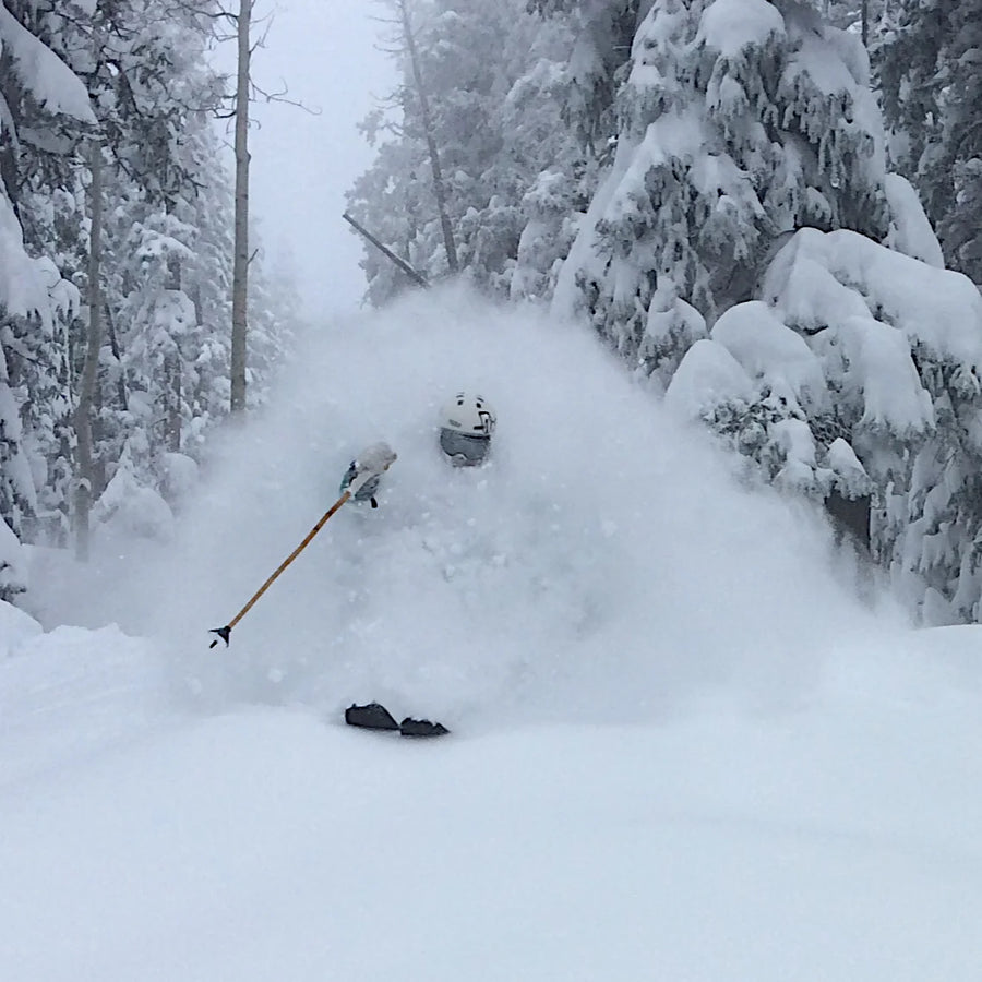 Gliding through deep powder in a snowy, forested landscape on the Icelantic Skis Nomad 112 Whiteout, the skier sends up a massive cloud of snow that partially obscures them from sight.
