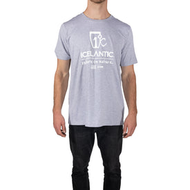A man stands against a white background wearing the Icelantic Logo Tee - Grey by Icelantic Skis and black jeans. Made from eco-friendly cotton, this ultra-soft unisex shirt combines comfort and style, featuring the "Icelantic return to nature" text on the front.