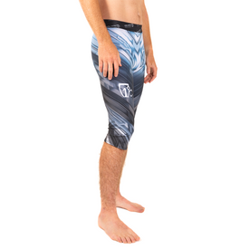 A man stands barefoot in profile, wearing the Icelantic 23/24 Men's WikMax Baselayer 3/4 Bottoms—crafted from WIKMAX fabric in a blue and gray pattern—that extend below the knee.