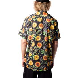 A person with light brown hair, dressed in a black cap and the Icelantic Skis Sunflower Party Shirt—showcasing vibrant Travis Parr-inspired sunflower and green leaf patterns—stands with their back to the camera against a white background. This short-sleeve shirt is made from eco-friendly recycled polyester, highlighting sustainable style.