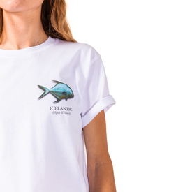 A person is wearing the Icelantic Permit Tee, a GOTS certified unisex t-shirt made from organic cotton. The white tee features a blue fish graphic and the text "ICELANTIC (Return To Nature)" on the upper left side. Only the lower face, chest, and one arm are visible. This shirt combines comfort with eco-conscious style.