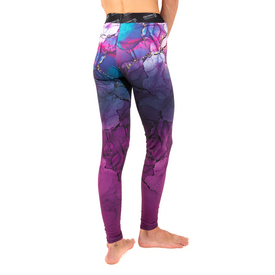 A person stands barefoot, wearing Icelantic’s 23/24 Womens WikMax Baselayer Full Bottoms. These stylish leggings, crafted from WIKMAX fabric, showcase a vibrant purple, blue, and pink marble-like pattern. The image highlights the legs, with only the lower portion of the wearer’s upper body visible.