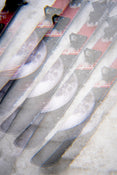 A close-up, double-exposed image of several Icelantic Skis Nomad 100 skis crossed over each other, featuring a moon graphic on their surfaces and a snowy background.
