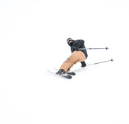 A skier carves a sharp turn on a snowy slope, leaning to one side with poles trailing behind, riding on Icelantic Skis’ Nomad 100 Whiteout against a pristine white backdrop.