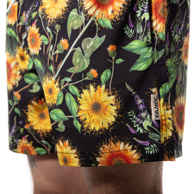 Close-up of a person's shorts featuring a vibrant sunflower and leaf pattern on a black background. The Sunflower Swim Trunks by Icelantic Skis offer eye-catching style, while their quick-dry design ensures all-day comfort. A small side tag displays the Icelantic Skis brand.