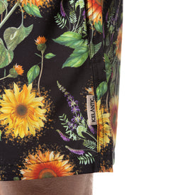 Close-up of vibrant floral-patterned fabric, predominantly showcasing sunflowers and green leaves, with a small ICELANTIC tag sewn into the seam. The fabric is from Icelantic Skis’ Sunflower Swim Trunks, designed for quick-dry performance and shown worn on a person's leg.
