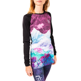 A woman wears the Icelantic 23/24 Womens WikMax Baselayer Top from the Riveter Collection, featuring a mountain and sky design in purple, blue, and white. She stands facing forward with her head partially out of frame.
