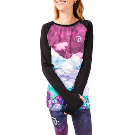 A woman smiles with arms crossed, wearing the Icelantic 23/24 Women's WikMax Baselayer Top and matching leggings in a vibrant mountain and abstract print, crafted from soft, high-performance WIKMAX fabric, against a white background.