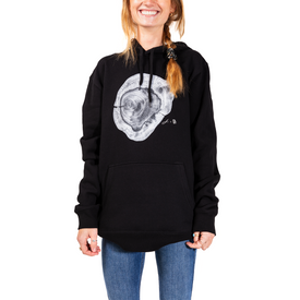 A person wearing a black Icelantic Yew Lineage Hoodie from the Jack Ludlam Backcountry Collection, featuring a white tree ring graphic on the front, standing and smiling with hands relaxed by their sides.