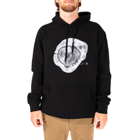 A person wearing the Icelantic Yew Lineage Hoodie—a black hoodie featuring a white tree ring graphic on the chest—and tan pants, standing against a white background.