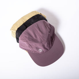 Three hats are stacked together: the front hat is a lightweight running cap in purple with small black dots and a white logo; the middle hat is the Camp Cap - Black by Icelantic Skis, featuring black dot details for a sleek appearance; and the back hat is a breathable quick-dry cap in beige with black dots. All hats are displayed on a white background.