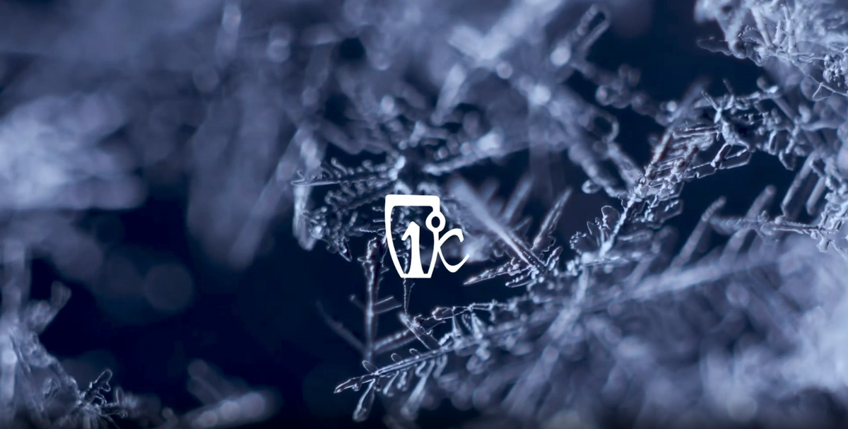 Close-up of intricate ice crystals or snowflakes with a white iced drink icon in the center, set against a dark, blurred background.