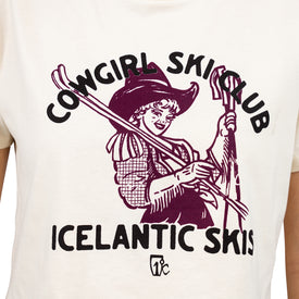 The Cowgirl Ski Club Cropped Tee by Icelantic features an illustration of a cowgirl in a hat holding ski poles, with "Cowgirl Ski Club" printed above and "Icelantic Skis" below, on a relaxed fit women's cropped tee in a light color.