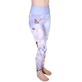 A person stands barefoot on a white background, with only their lower body visible, wearing Icelantic’s 22/23 Maiden Legging—high-waisted pastel purple leggings adorned with butterfly and cloud motifs, featuring a comfortable high-waist waistband and crafted from breathable wicking fabric.