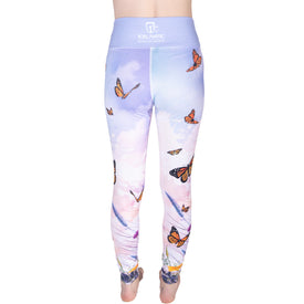 A person is shown from the back wearing Icelantic 22/23 Maiden Leggings in a pastel Icey colorway, decorated with orange butterfly and purple flower designs. These high-waisted leggings feature the Icelantic brand logo on the waistband and are crafted from moisture-wicking fabric for stylish comfort during everyday wear.