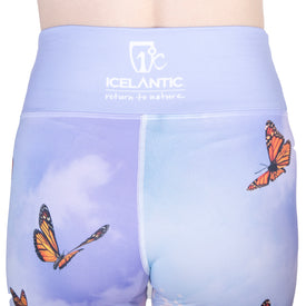 Wearing the Icelantic 22/23 Maiden Legging, which showcases a blue sky and orange butterfly design, these high-waisted leggings are crafted from moisture-wicking fabric and feature "Icelantic return to nature" printed in white on the secure waistband.