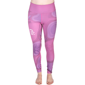 A person wearing Icelantic’s 22/23 Mystic Legging—crafted from Hyper Wiking WIKMAX Fabric, with a high-waist waistband, a pink and purple pattern, and a white logo on the left hip—stands barefoot against a white background.
