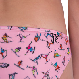 Close-up of a person wearing the Icelantic Skier MTN Bikini Bottom in pink, an ethically sourced swimwear piece adorned with vibrant illustrations of skiers and snowboarders in action. The fabric is finished with a small black Icelantic logo near the waistband, combining style and peace of mind.