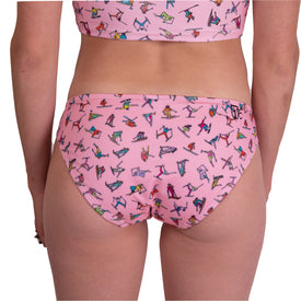 A person wearing the Icelantic Skier MTN Bikini Bottom - Pink, featuring a colorful yoga pose print, is shown from the back with part of a matching top visible—an ideal choice for those seeking an ethically sourced or playful, full coverage swim bottom.
