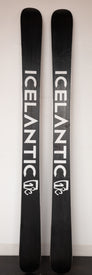 A pair of black 20/21 Nomad 115 Used Demo skis by Icelantic stand upright against a wall, each featuring the brand's name "ICELANTIC" in bold white vertical text with a small logo beneath—an outstanding big mountain freeride ski ideal as demo skis or for your next adventure.