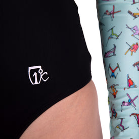 Close-up of a person wearing the Icelantic Skier LS One Piece, featuring black swim bottoms with a white 17°C logo and chlorine-resistant fabric, alongside another person in colorful patterned leggings against a white background.