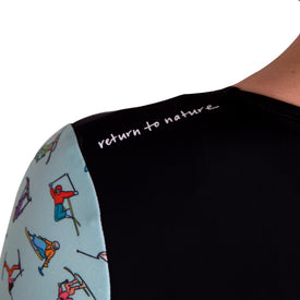Close-up of the Icelantic Skier LS One Piece, a long sleeve swimsuit featuring colorful cartoon skiers on the sleeve and "return to nature" in white text across the black shoulder. This suit offers both UV protection and a chlorine resistant finish.