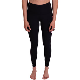 A person stands barefoot, wearing Icelantic's Skier Pocket Legging in Black/Pink—high-waisted leggings crafted from eco-friendly recycled polyester. A cropped top completes the outfit. Only the torso and legs are visible; the face is not shown. Relaxed hands rest at the sides, adorned with rings on the fingers.