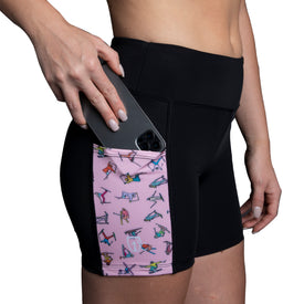 A person places a black smartphone into the pink side pocket of the Icelantic Skier Pocket Short - Black/Pink, crafted from recycled fabric and decorated with colorful workout illustrations.