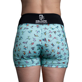 A person is seen from behind wearing the Icelantic Skier Pocket Short - Mint, featuring a playful skier pattern on light blue fabric. The shorts have a black waistband displaying the white “Icelantic return to nature” text and are made from recycled materials for an eco-friendly finish.
