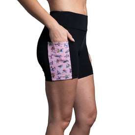 A person wears the Icelantic Skier Pocket Short in Black/Pink, women's biker shorts made from recycled fabric, featuring a pink side pocket with colorful abstract designs, standing against a white background.