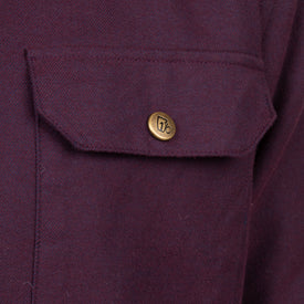 Close-up of the Sherpa Lined Jacket by Icelantic, highlighting a maroon fabric pocket with a flap and a brass button featuring an engraved design. The heavyweight material’s texture and stitching are clearly visible.