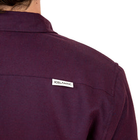 A close-up of a person wearing the Sherpa Lined Jacket from Icelantic, viewed from the back. A small rectangular tag near the shoulder displays "Icelantic," showcasing the brand's dedication to sustainable apparel. The jacket's collar and upper back are visible against a white background.