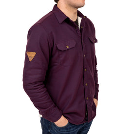 A man wearing the Icelantic Sherpa Lined Jacket in maroon—with chest pockets and a patch on the left sleeve—stands with his hands in his jeans pockets, facing slightly to the right.