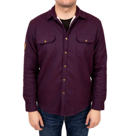 A man wearing the Icelantic Sherpa Lined Jacket—a dark purple heavyweight style featuring two chest pockets—paired with blue jeans stands facing the camera, his head partially out of frame.