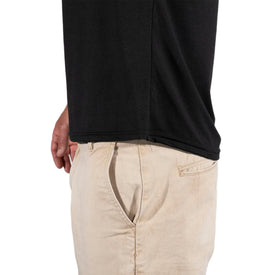 Wearing the Icelantic Skis SoftTECH T in black—a comfortable, antimicrobial t-shirt—and beige pants, a person stands sideways with one hand in their pocket against a plain white background.