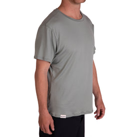 A man is wearing the Icelantic SoftTECH T - Greenish, a comfortable short-sleeve t-shirt, along with black pants. He stands against a white background, facing slightly to the right with his face partially out of view.