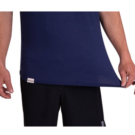 A person wearing the Icelantic SoftTECH T in Navy and black pants stretches the bottom edge of the shirt outward with their right hand. Only their torso and arms are visible.