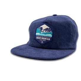 The Rocky Mountain Corduroy Hat by Icelantic Skis is a blue snapback hat crafted from corduroy, featuring a hexagon patch with mountain artwork and the text "Rocky Mountain" and "National Park Collection" on the front. This stylish hat includes an adjustable snapback closure and is displayed against a plain white background.