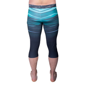 A person stands barefoot, facing away, wearing the Icelantic 22/23 Mens WikMax Baselayer 3/4 Bottom. These athletic leggings feature a teal and black landscape-inspired pattern, a visible waistband, and are made with WIKMAX fabric for enhanced comfort.